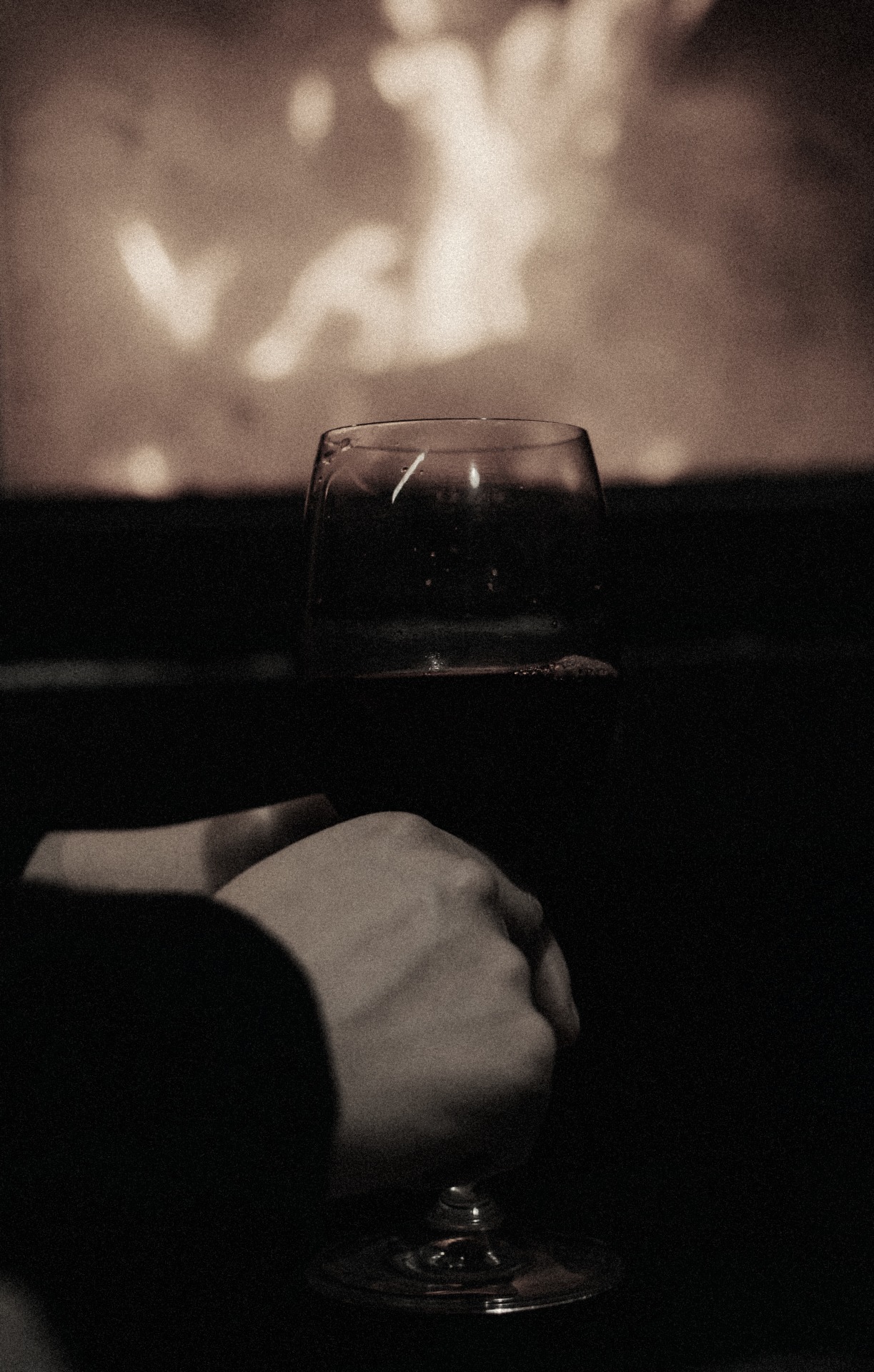 A hand holding a glass of red wine in front of a fire